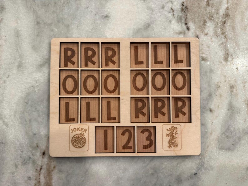 May include: A rectangular light-colored wooden game board featuring a grid of eighteen squares with the letters R, O, and L engraved in dark brown. Below the grid are three additional squares labeled 1, 2, and 3, flanked by a Joker icon and a dragon icon.