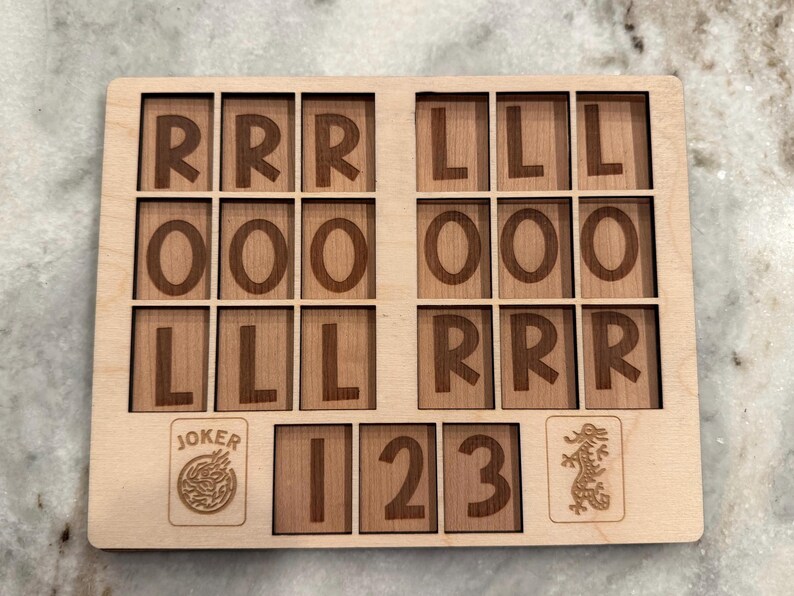 May include: A rectangular light-colored wooden board featuring a grid of engraved letters and numbers. The top section contains three rows of letters R, O, and L. The bottom section displays a Joker icon, the numbers 1, 2, 3, and a dragon icon.