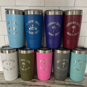May include: A collection of insulated tumblers in various colors, including blue, green, and pink. Each tumbler has a silver lid and features the text "BIRTHDAY SPREE ARUBA 2023" with a decorative element like a crown or palm tree.