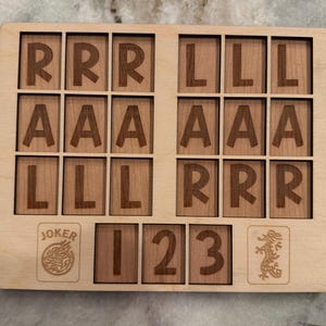 May include: Wooden game board with engraved letters, numbers, and card symbols. The board features the letters R, A, and L, along with the numbers 1, 2, and 3. Includes a "JOKER" card and a dragon symbol.