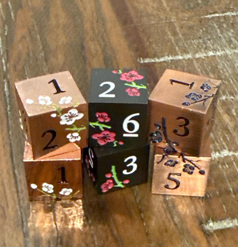 May include: Six wooden dice with floral designs and numbers. The dice are copper and black, with white and red floral accents. Numbers are painted in white. The dice are arranged in a small pile.