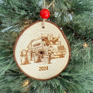 May include: A wooden Christmas ornament featuring a cartoon image of a man driving a garbage truck with other people in trash cans. The text "TRUMP MANAGEMENT" and "2024" are also included on the ornament.