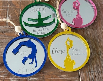 May include: Four circular mirrored ornaments with colored acrylic frames in green, pink, blue, and yellow. Each features a cutout of a cheerleader in a different pose, personalized names like Avery, Caroline, Charlee, and Clara, and years like 2024.