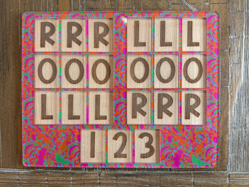 May include: A rectangular board featuring a vibrant, multi-colored psychedelic pattern in shades of pink, orange, and green. The board contains multiple square wooden tiles engraved with the letters R, L, O, and the numbers 1, 2, and 3.