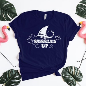 May include: A navy blue t-shirt with a white shark fin and bubbles graphic. The text "Bubbles Up" is printed in white below the graphic.