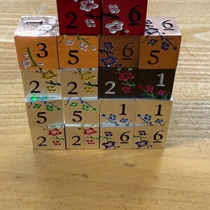 May include: A stack of wooden dice with floral designs and numbers. The dice are painted in various colors, including red, orange, brown, and cream. Each die face displays a number from 1 to 6.