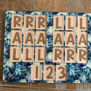 May include: A rectangular wooden puzzle board featuring a dark blue and teal floral pattern border. The board contains square wooden tiles engraved with the letters R, L, and A, and the numbers 1, 2, and 3, arranged in a grid-like layout.