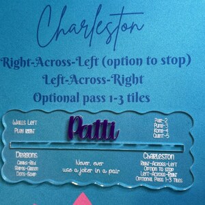 May include: A clear acrylic game piece with the name "Patti" in purple script. The piece has text that reads "Charleston" and game instructions. The background is a textured blue surface.