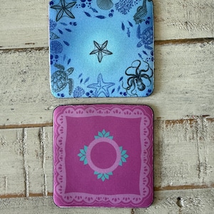 May include: Two square coasters. The top coaster has a blue gradient background with starfish, sea turtles, and other sea life. The bottom coaster is magenta with a teal and white circular design.