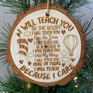 May include: Wooden Christmas ornament with a brown wood grain finish. The ornament is round and has a string for hanging. The ornament has a white design with the text "I Will Teach You" and a quote about teaching in the classroom, on Zoom, and in a house with a mouse.
