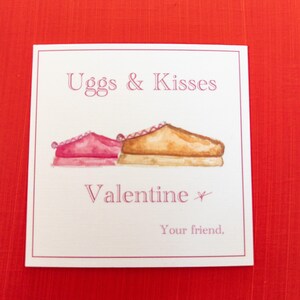 May include: A Valentine's Day card with the text "Uggs & Kisses" and "Valentine". The card features watercolor illustrations of two Ugg-style boots, one pink and one tan, on a white background with a red border.