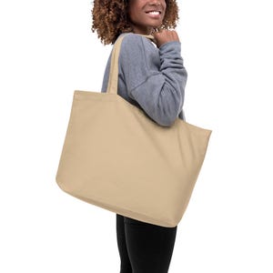 Puede incluir: Una bolsa de lona grande de color beige con asas largas. La bolsa está vacía y la está sujetando una persona.