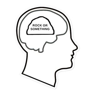 May include: A black and white line drawing of a person's head with the words "Rock or Something" inside the brain.
