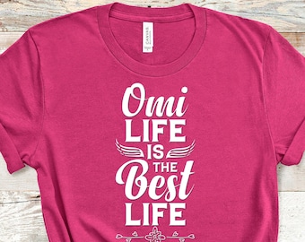 May include: Pink t-shirt with white text that reads "Omi Life is the Best Life" with wings and a floral design.