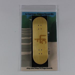 May include: A wooden fingerboard with the text "4 Corner Fingerboards" and "etsy.com/shop/4CornerFingerboards" printed on it. The fingerboard is in a clear plastic bag.