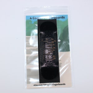 May include: A black fingerboard with a brown graphic design. The fingerboard is packaged in a clear plastic bag with a white card that says "4 Corner Fingerboards" and "etsy.com/shop/LCFingerboards".