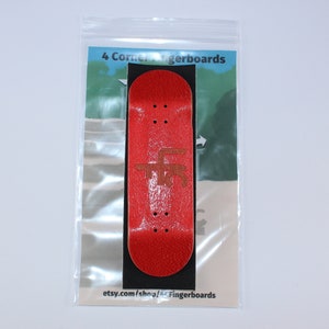 May include: A red fingerboard with a brown graphic on it. The fingerboard is in a clear plastic bag with a white background. The text "4 Corner Fingerboards" is printed on the bag.