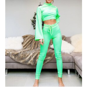 Pode incluir: Um conjunto de duas pe&ccedil;as verde brilhante com uma blusa de manga comprida e cal&ccedil;as combinando. A blusa tem gola alta e as cal&ccedil;as t&ecirc;m cintura com cord&atilde;o.