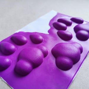 May include: Purple silicone mold with two paw prints. Each paw print has five raised bumps.