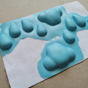 May include: A close-up of a light blue fabric with raised, textured shapes. The shapes are in the form of paw prints and clouds.