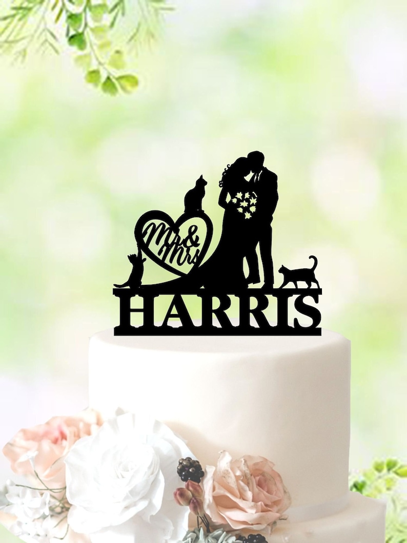 May include: Black silhouette cake topper featuring a bride and groom kissing, two cats, a heart with "Mr. & Mrs. Harris" written inside, and the last name "HARRIS" below.