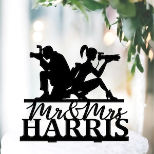 Puede incluir: Topper de pastel en silueta negra de una novia y un novio sosteniendo cámaras con el texto "Mr & Mrs HARRIS" debajo.