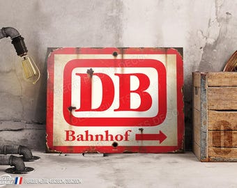 Puede incluir: Un letrero metálico rectangular rojo y blanco con las letras "DB", la palabra "Bahnhof" y una flecha. El letrero tiene un aspecto vintage y desgastado. Mide 40 cm x 30 cm.