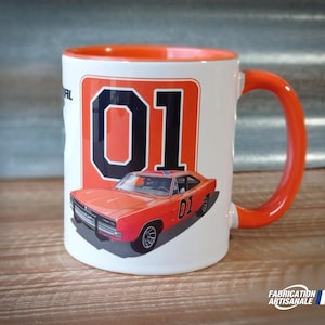Op de afbeelding: Witte keramische mok met een oranje rand en handvat. De mok heeft een afbeelding van een feloranje Dodge Charger uit 1969 met het nummer "01" in zwart op een oranje achtergrond.