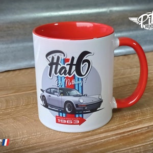Peut inclure: Mug en céramique blanche avec intérieur et poignée rouges. Le mug présente un graphique d'une Porsche 911 argentée avec le texte "Flat 6... Or Nothing!" et "Production Start 1963".