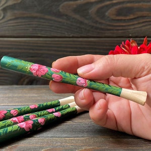 May include: Set of four wooden cigarette holders painted with pink flowers on a green background. The holders are approximately 6 inches long.
