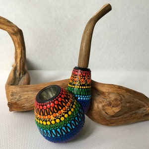May include: A rainbow colored wooden smoking pipe with a black bowl and a wooden stem. The pipe is decorated with a mandala pattern.
