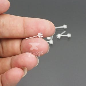 May include: A small silver stud earring post with a four-prong setting designed to hold a gemstone. The earring features a thin metal pin and a notched end for secure fastening. Several additional identical silver earring posts are visible nearby.