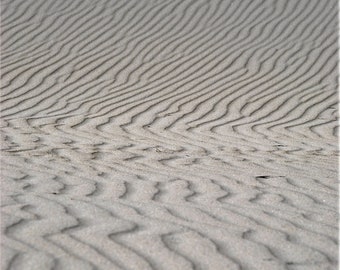 May include: A close-up of a sandy beach with wavy patterns created by the wind.
