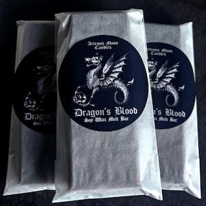 May include: Three white paper bags with black labels. Each label features a black and white illustration of a dragon with the text "Artemis Moon Candles" and "Dragon's Blood Soy Wax Melt Bar".