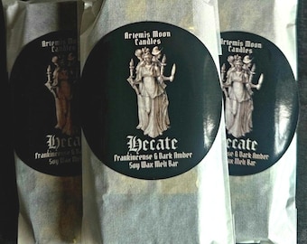 May include: Three white paper bags with black labels. Each label features a black and white illustration of a woman holding torches and a sword. The text on the label reads "Artemis Moon Candles" and "Hecate Frankincense & Dark Amber Soy Wax Melt Bar".