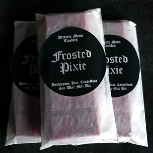 May include: Three individually wrapped soy wax melt bars in a frosted purple colour. Each bar has a black circle label with white text that reads "Artemis Moon Candles" and "Frosted Pixie" with the scent description "Bubblegum, Pear, Candyfloss".