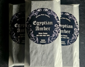 May include: Three wrapped soy wax melt bars labeled "Egyptian Amber" with a dark blue and white circular sticker. The sticker reads "Artemis Moon Candles" and "Warm Amber Soy Wax Melt Bar". The packaging is white and the background is dark.