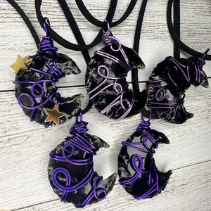 May include: Five black obsidian crescent moon pendants wrapped in purple wire. Some pendants have gold star accents. The pendants are on black cords.