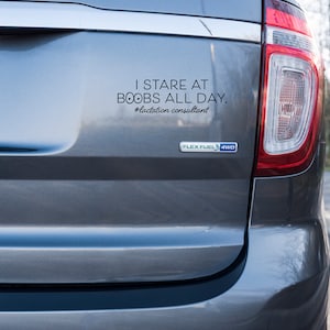 May include: A gray vehicle's rear with a bumper sticker that reads, "I STARE AT BOOBS ALL DAY. #lactation consultant." The vehicle has a Flex Fuel 4WD emblem and a license plate. The taillight is visible.