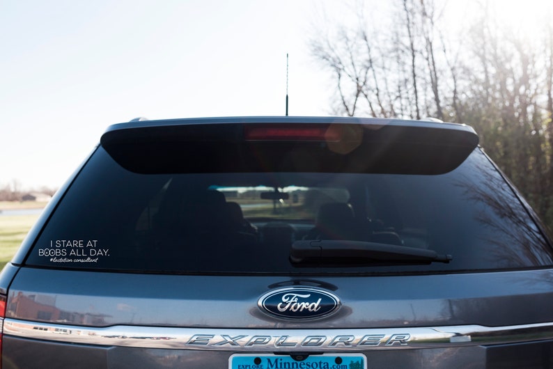 May include: Rear view of a gray Ford Explorer SUV with a sticker on the back window. The sticker reads "I STARE AT BOOBS ALL DAY." and "#lactation consultant."