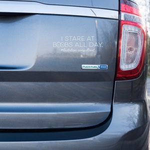 May include: Rear view of a gray SUV with a bumper sticker that reads "I STARE AT BOOBS ALL DAY. #lactation consultant". The vehicle has a Flex Fuel 4WD emblem.