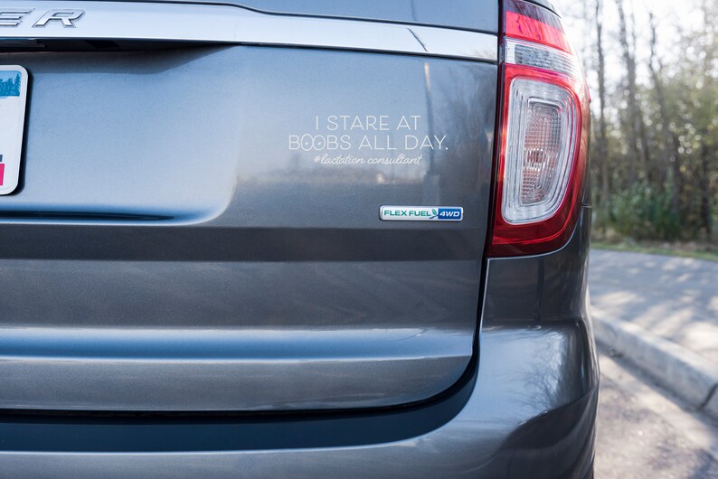 May include: Rear view of a gray SUV with a bumper sticker that reads "I STARE AT BOOBS ALL DAY. #lactation consultant". The vehicle has a Flex Fuel 4WD emblem.