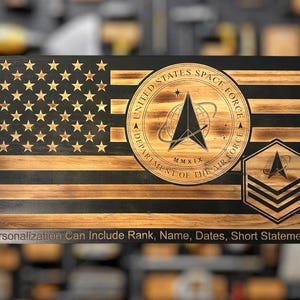 May include: Wooden American flag with the United States Space Force emblem and a rank insignia. The flag features laser-cut stars and stripes, with the Space Force logo in a circular design. Text at the bottom reads: Personalization Can Include Rank, Name, Dates, Short Statement.