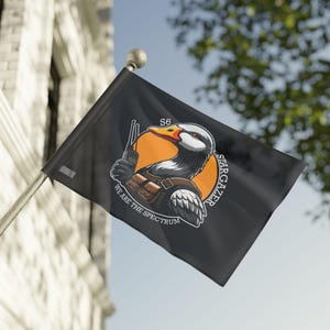 May include: Black flag featuring a cartoon duck with a radio, wearing a brown harness, and set against an orange circle. The flag has the text "S6", "STARGAZER", and "WE ARE THE SPECTRUM". The flag is waving in the wind.