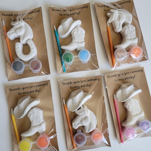 May include: Six party favor sets featuring cowboy-themed paintable figurines, including a horse head, cowboy hat, and boot. Each set includes paint pots and a paintbrush. The text "Thank you for coming to my party!" is printed on the packaging.