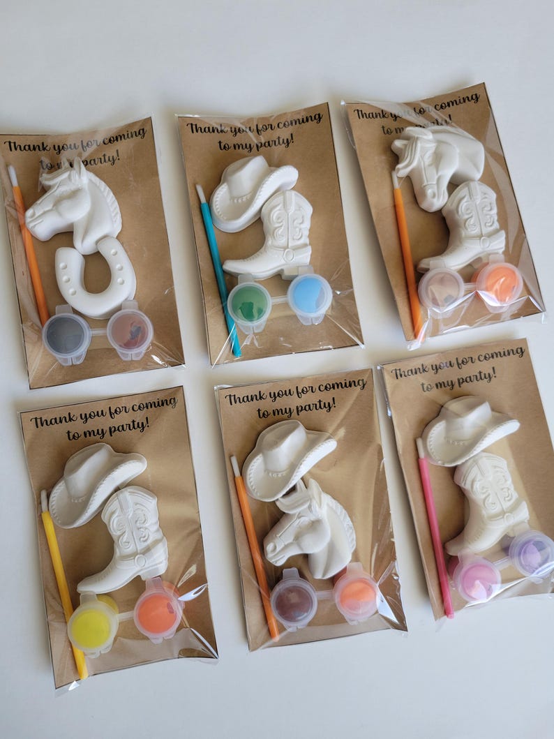 May include: Six party favor sets featuring cowboy-themed paintable figurines, including a horse head, cowboy hat, and boot. Each set includes paint pots and a paintbrush. The text "Thank you for coming to my party!" is printed on the packaging.