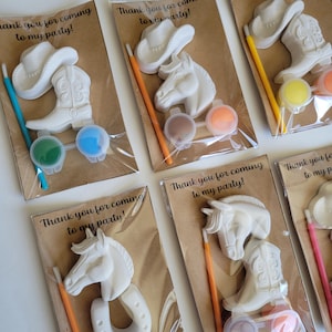 May include: White cowboy-themed paint kits. Each kit includes a cowboy hat, horse head, horseshoe, and cowboy boot, along with paint and a brush. The text "Thank you for coming to my party!" is printed on the packaging.