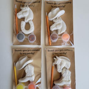 May include: Four party favor sets with a cowboy theme. Each set includes a white horse, horseshoe, cowboy hat, or cowboy boot, paint pots, and a paintbrush. The text "Thank you for coming to my party!" is printed on the packaging.