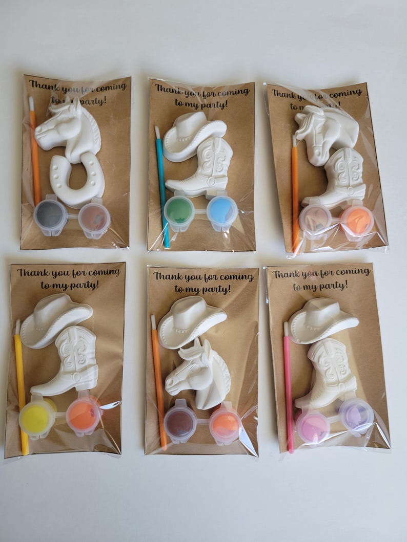 May include: Six party favor sets with a cowboy theme. Each set includes a white plaster horse head, horseshoe, cowboy hat, or boot, paint pots, and a paintbrush. The sets are packaged in clear plastic bags with a brown paper backing. Text on the packaging reads "Thank you for coming to my party!"
