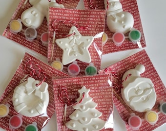 Pode incluir: Cinco sacos de plástico transparente individuais com ornamentos de Natal em cerâmica branca em forma de rena, boneco de neve, estrela, coroa, árvore e Pai Natal. Cada saco inclui um pincel pequeno e três potes de tinta vermelha, verde e amarela.